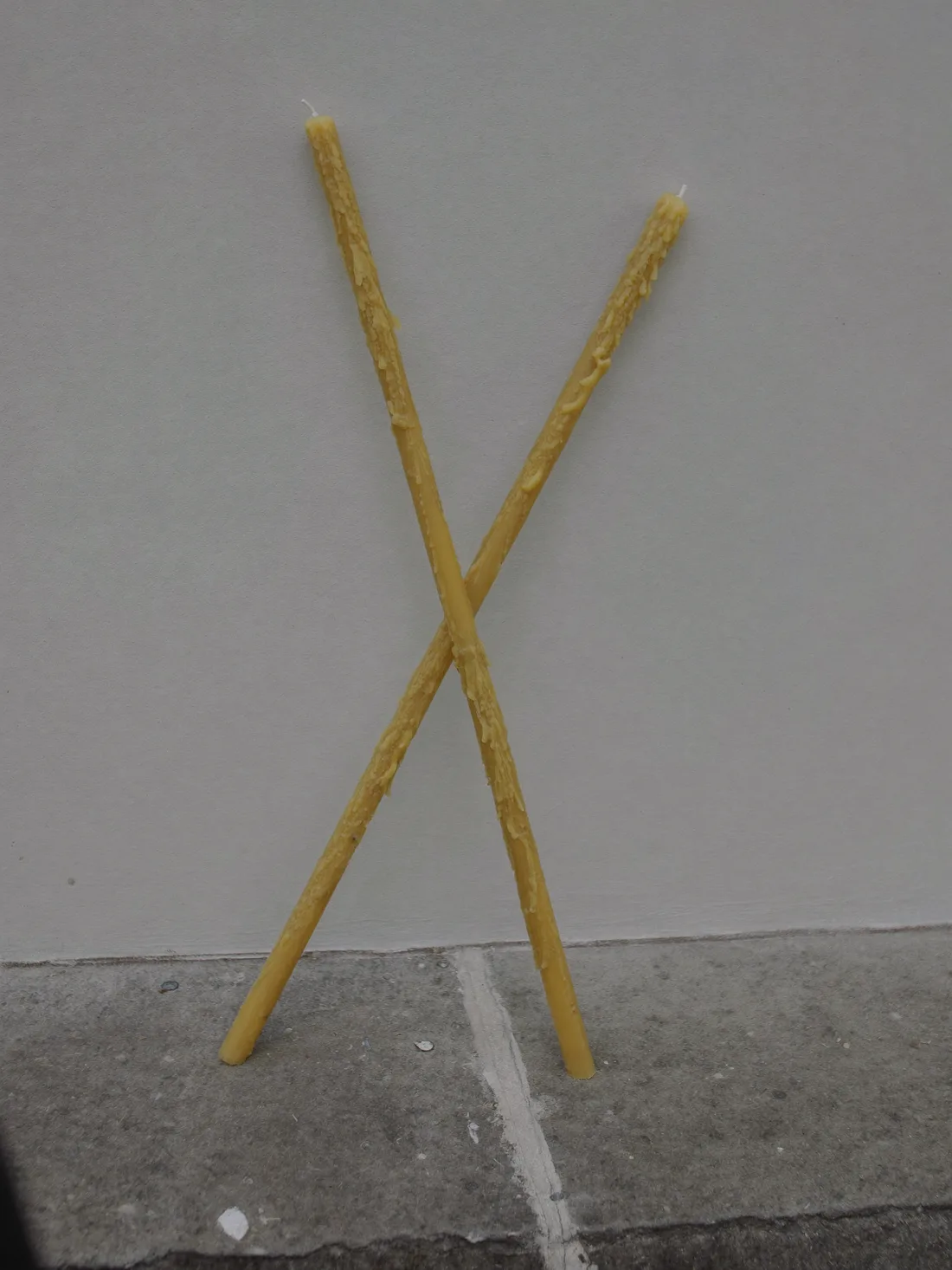 Pair of beeswax taper candles leaning against a pale wall