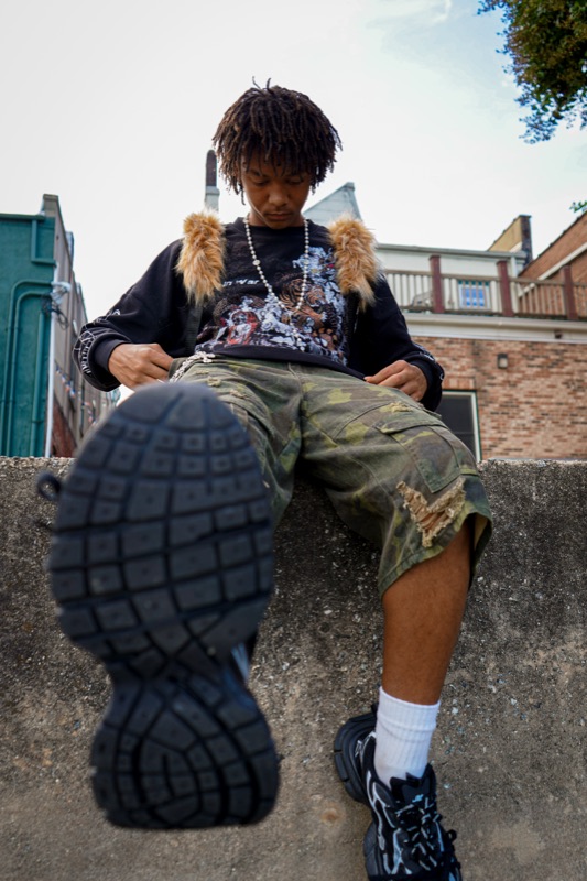 Low-angle portrait of a young man seated on a concrete ledge, sneaker sole filling the foreground.